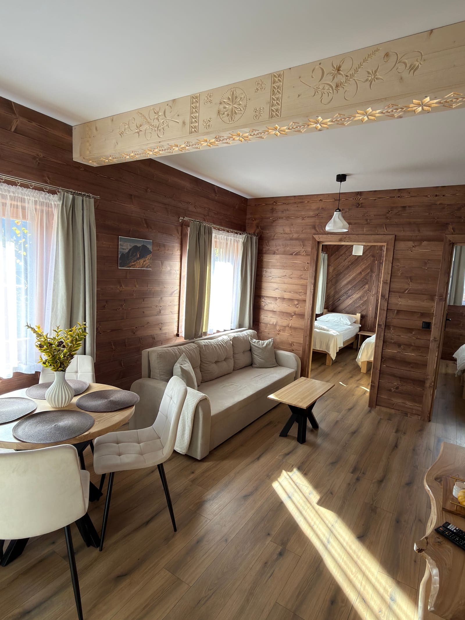 Jasny salon z sofą, stołem i drewnianymi ścianami w apartamencie w Nowem Bystrem