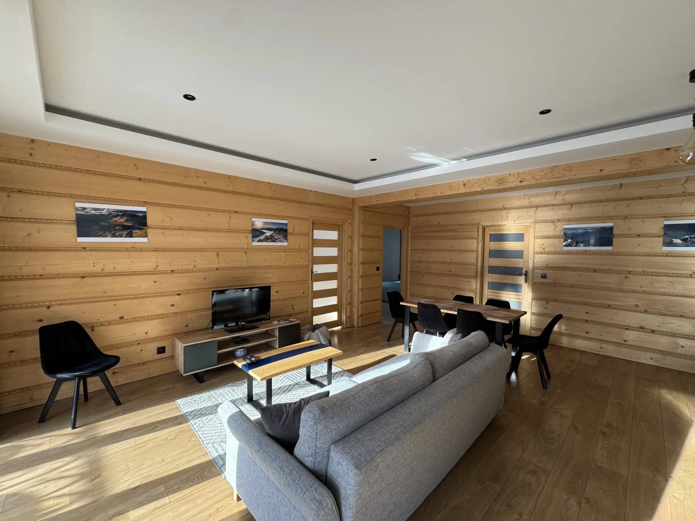 Salon apartamentu wyłożony jasnym drewnem, z sofą i drewnianym stołem